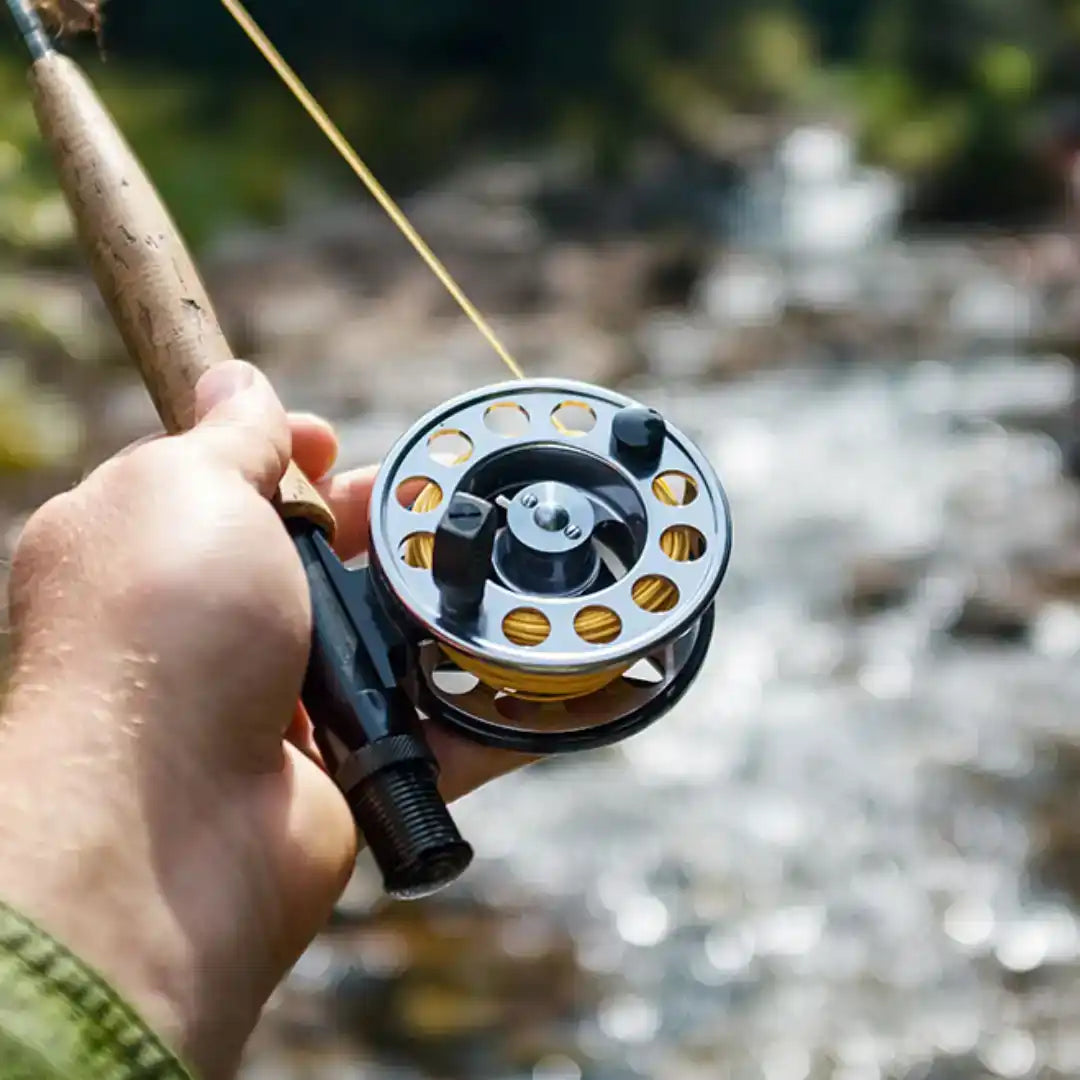 A person’s hand holding a fly fishing rod and reel with yellow line.