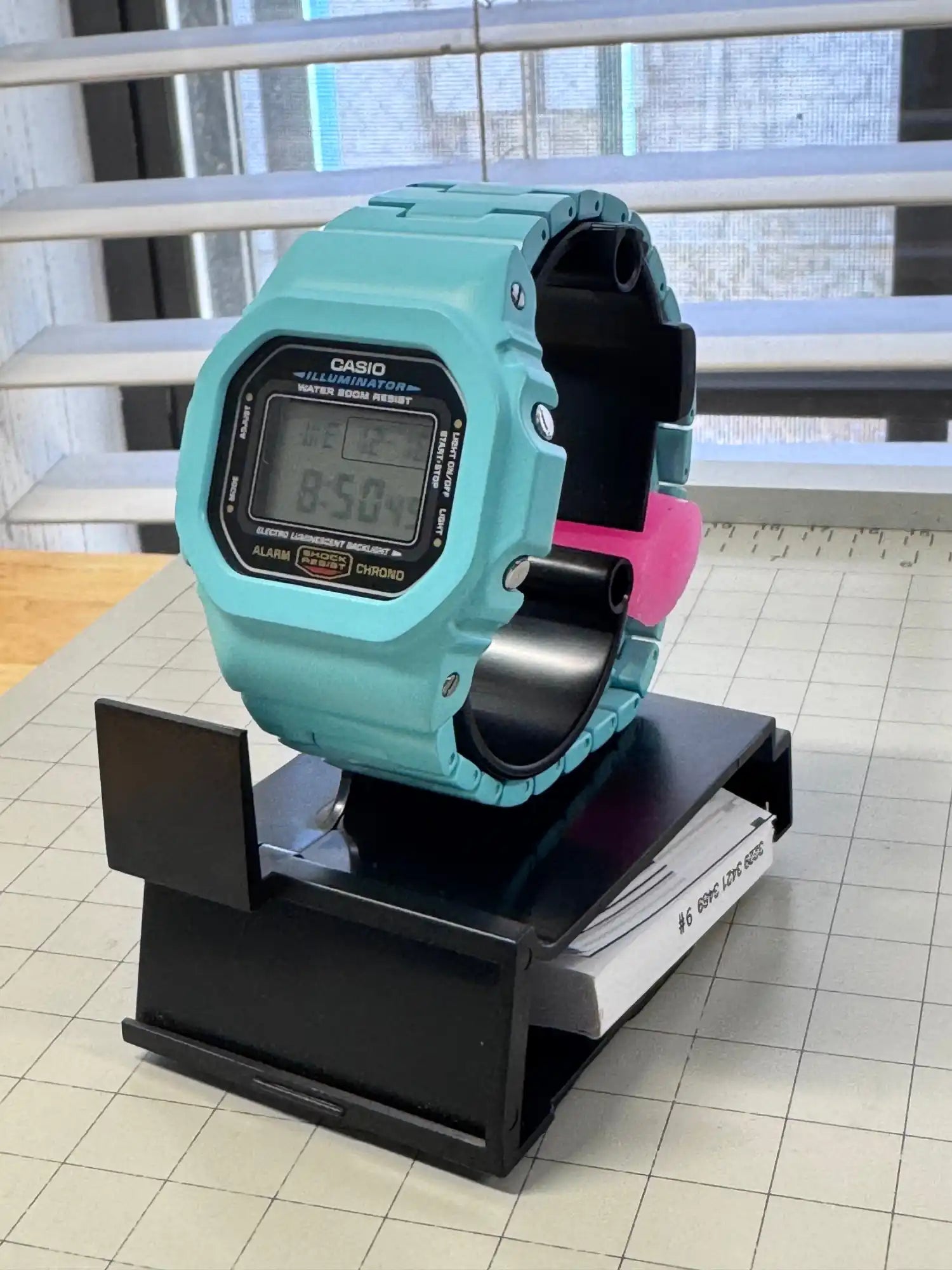 Turquoise digital watch on display stand.