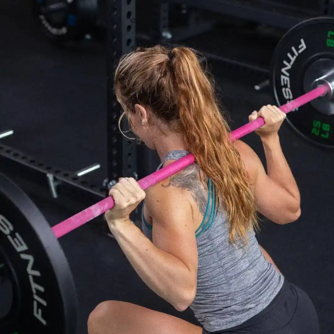 A woman performing a barbell squat with a pink-wrapped bar.